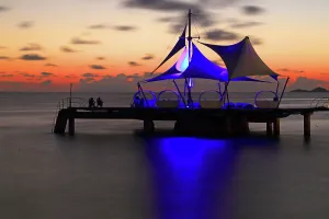 Watercraft Prints: Sunset view over water with a pier and structure at Coco de Mer resort on Praslin Island in Seychelles
