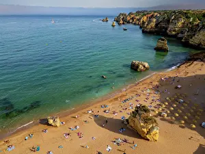 Swimming Prints: Sunset views of beach cliffs by the sea in Algarve showing people enjoying time on the sand