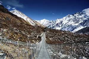 Snowcapped Prints: Suspension bridge leading into the snowy expanse of Langtang Valley with clear views of Gangchempo‚Äôs striking summit
