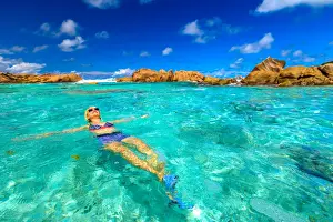 Arms Outstretched Prints: Swimming pool at Anse Cocos with woman in bikini lying in turquoise water of natural