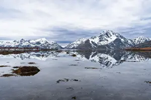 Awe Inspiring Prints: Tall mountains with snowy peaks reflecting in the calm water of the fjord at high tide with scenic clouds