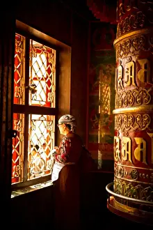Prayer Wheel Prints: A Tibetan woman stands next to a large prayer wheel of the temple of Boudhanath Stupa