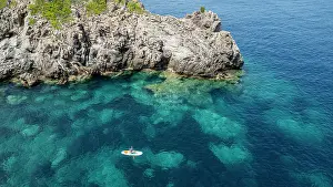 Fitness Prints: Tourist enjoys stand-up paddleboarding in turquoise waters near rocks in Mallorca