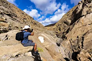 Photographer Prints: Tourist photographing canyons with smartphone sitting on rocks at Barranco de las Penitas