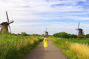 Kinderdijk Prints: A tourist walks in the midst of Unesco Windmills of Kinderdijk during sunset