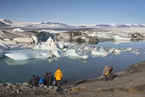 Touris ts viewing icebergs in Jokuls arlon glacial lagoon, Oraefajokull glacier in the dis tance