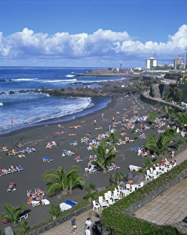 Black Sand Prints: Tourists on volcanic sand beach at Playa Jardin, with San Felipe Castle