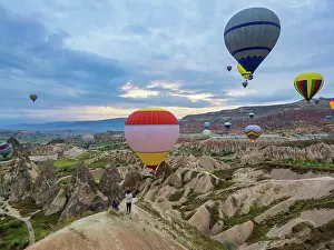 Cappadocia Prints: Tourists watch hot air balloons flying over Cappadocia at sunrise in Turkey while enjoying the scenic views