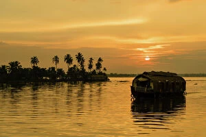 Lagoon Gallery: A traditional houseboat moves past the setting sun on the Kerala Backwaters, Kerala