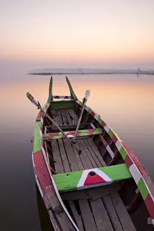 Rowing Boat Prints: Traditional rowing boat moored on the edge of flat calm Taungthaman Lake at dawn with the colours of the sky reflecting