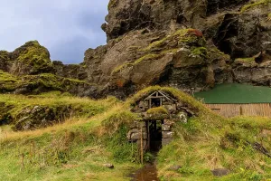 Grassland Prints: Traditional turf hut built against a cliff face showcases Icelandic shelter construction near Seljalandsfoss