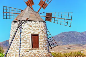 Mountaintop Prints: Traditional windmill stands in Fuerteventura under bright sun with clear blue sky and mountains in background