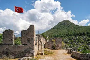 Turkish Prints: Turkish flag waves over the ruins of Kayakoy ghost town surrounded by lush mountains in Turkey