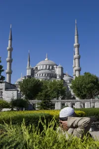 Hands Clasped Prints: Turkish man with traditional headware relaxing in Sultanahmet Square in front of the Blue Mosque