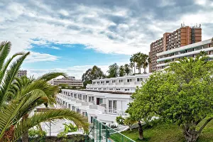 Apartment Building Prints: Urban landscape with modern apartment buildings surrounded by lush greenery under a cloudy sky in Los Cristianos