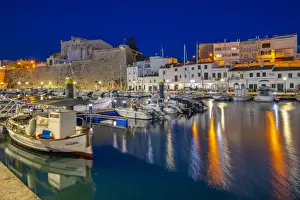 Menorca Prints: View of boats in marina overlooked by whitewashed buildings at dusk