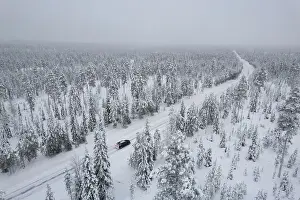 Akaslompolo Prints: View from above of a car travelling icy road in the middle of the frozen forest covered with snow