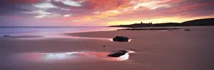 View along Embleton Bay at sunrise, with silhouette of Dunstanburgh Castle in the distance