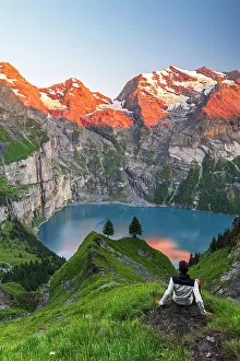 Mid Adults Prints: View of a hiker resting in front of the Oeschinensee lake surrounded by snowy peak at sunset