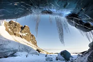 South Iceland Prints: View from ice cave towards sunlit mountains with icicles hanging from cave entrance