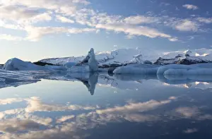 View over Jokulsarlon, a glacial lagoon at the head of the Breidamerkurjokull Glacier, towards icebergs and snow-capped mountains, with reflections in the calm water of the lagoon on a winters afternoon, on the edge of the Vatnajokull National Park, South Iceland, Iceland, Polar Regions