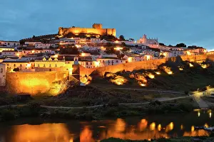 Alentejo Prints: View of Mertola above the Guadiana River during evening with lights from buildings shining brightly