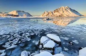 View of the mountains of Gymsoya (Gimsoya) from Smorten reflected in the clear partially frozen sea