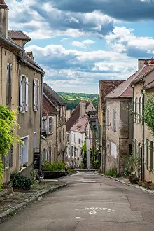 Quaint Prints: View down a narrow street in Vezelay with stone houses and green landscape under a blue sky in France