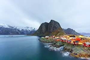 Northern Prints: View of red rorbu cabins by the water near a mountain in Lofoten Islands