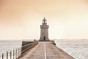 Route Prints: View of Saint Peter Port Lighthouse at sunset over the pier in Guernsey Channel Islands with stone pathway leading into