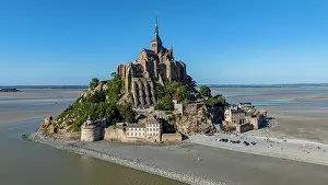 Visitors Prints: View showing Mont St. Michel surrounded by water and sand at low tide in France with clear blue sky above