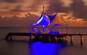 Retreat Prints: View of sunset at Coco de Mer resort with lit structures on the pier at Praslin Island in Seychelles