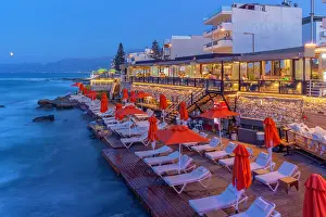 Chairs Prints: View of taverna with chairs and red umbrellas by the sea at dusk in Crete