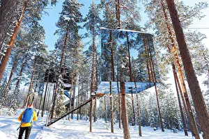 Mirror Prints: View of a tourist admiring the cube shaped room with mirror wall inside a boreal forest covered with ice and snow