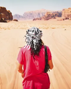 Back view of traveler wearing keffiyeh walking in Wadi Rum desert, Jordan, with red sand dunes and dramatic rock formations view traveler wearing keffiyeh walking wadi rum desert