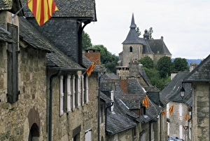 Limousin Prints: View along village street to church, with colourful flags, Turenne, Correze