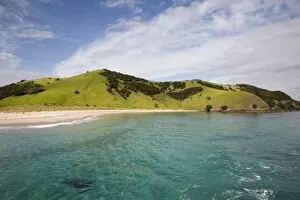 View back to Waewaetorea Island recreational reserve with sandy beach across clear green blue sea on Pacific coast