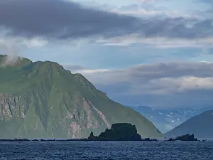 Uninhabited Prints: Views of the rocky Baby Islands in the Aleutian Islands of Alaska with mountains in the background