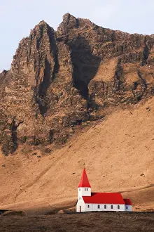 Enjoyment Prints: Vik Church stands alone against a backdrop of towering mountains in the landscape of Iceland