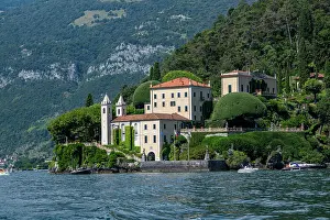 Watercraft Prints: Villa del Balbianello sits by the shore of Lake Como with green hills in the background and boats in the water
