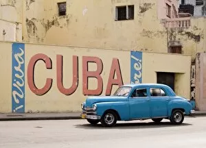 Automobile Collection: A vintage 1950s American car passing a Viva Cuba sign painted on a wall in cental Havana, Cuba