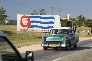 Cuban Prints: A vintage 1950s American Chevrolet on the road near Trinidad passing a colourful revolutionary road sign