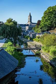 Creek Prints: Visitors enjoy a sunny day by the river in a town in France with historic buildings and trees in the background