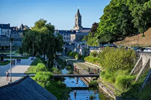 Clock Prints: Visitors walk near the river and buildings on a sunny day in a French town with a historical clock tower