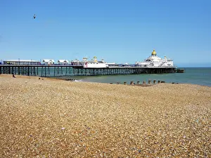 Vacationers Prints: Visitors walk on shingle beach near pier in Eastbourne with clear skies and calm waters during daytime in East Sussex