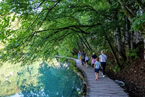 Footpath Prints: Visitors walk along the wooden path through Plitvice Lakes National Park surrounded by green trees in Croatia