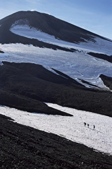 Volcanoe Prints: Walkers on snow field below steaming summit cone