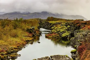 Channel Prints: Water channel flows through volcanic rock at Thingvellir with clouds over Iceland's rift valley