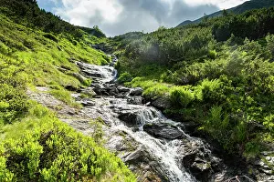 Freshness Prints: Water flows down rocks in a green landscape with hills and clouds in Romania's mountains