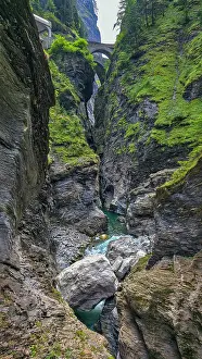 Fresh Prints: Water flows through rocky canyon as bridge spans above in Switzerland during daylight hours